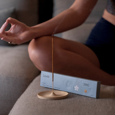 Person meditating cross-legged beside a burning Looshi Calm incense stick and its powder blue box