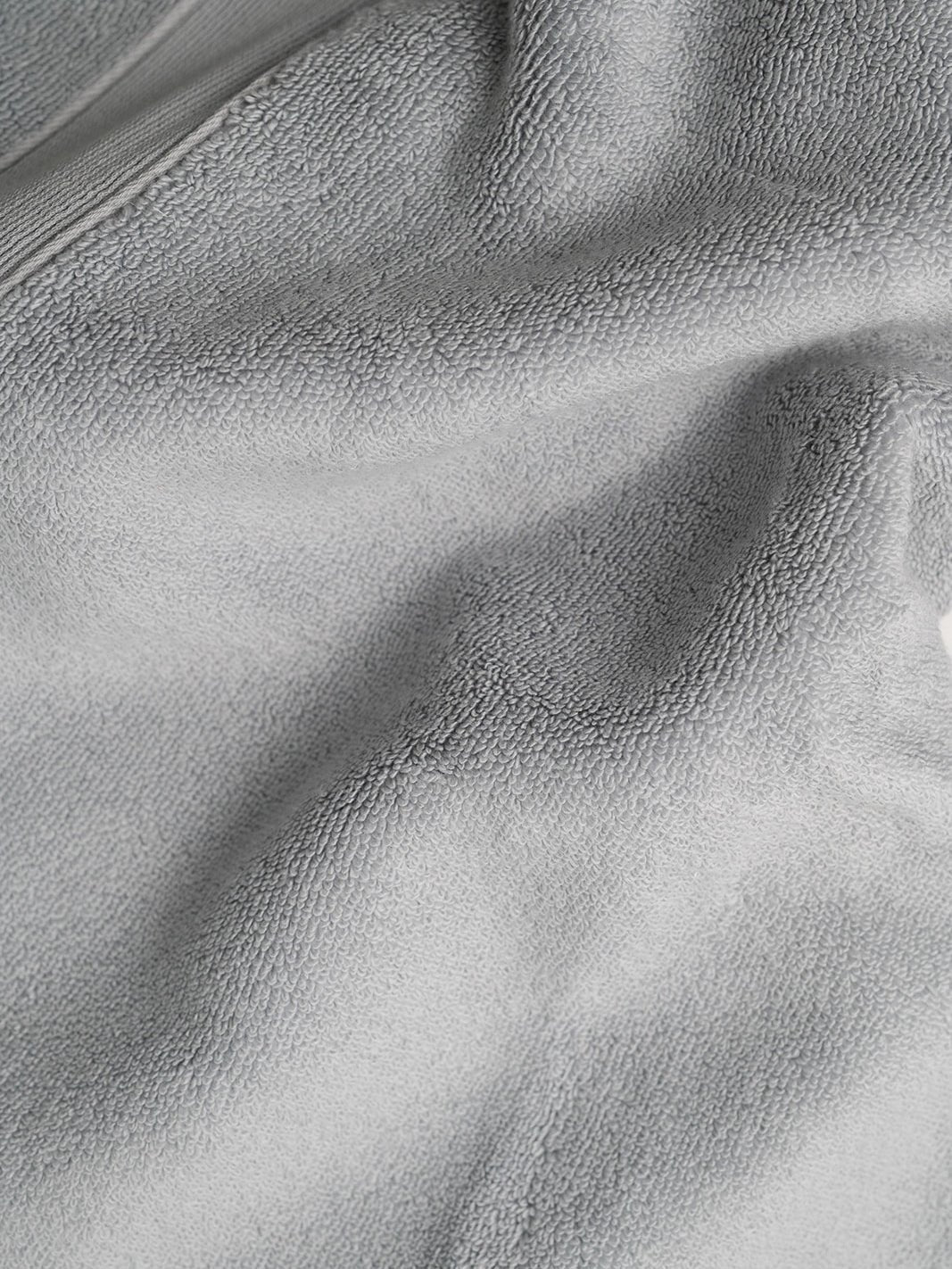 Close-up of light gray bath sheet fabric gathered into soft folds, showing its dense looped texture and part of the woven border.