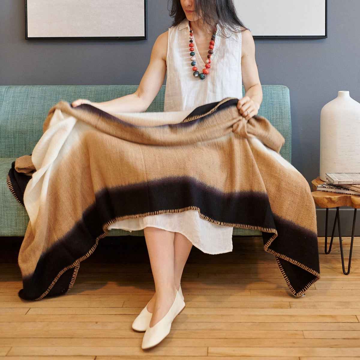 Woman seated with the Siro Brown merino throw spread across her lap, displaying its large color-block design