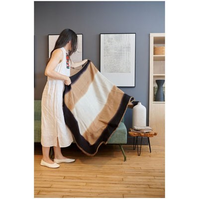 Woman standing and holding the Siro Brown throw open to display its full size, cream center and dark borders