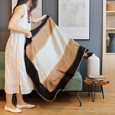 Woman holding the Siro Brown handwoven throw wide, showing its warm neutral color blocks and stitched edging