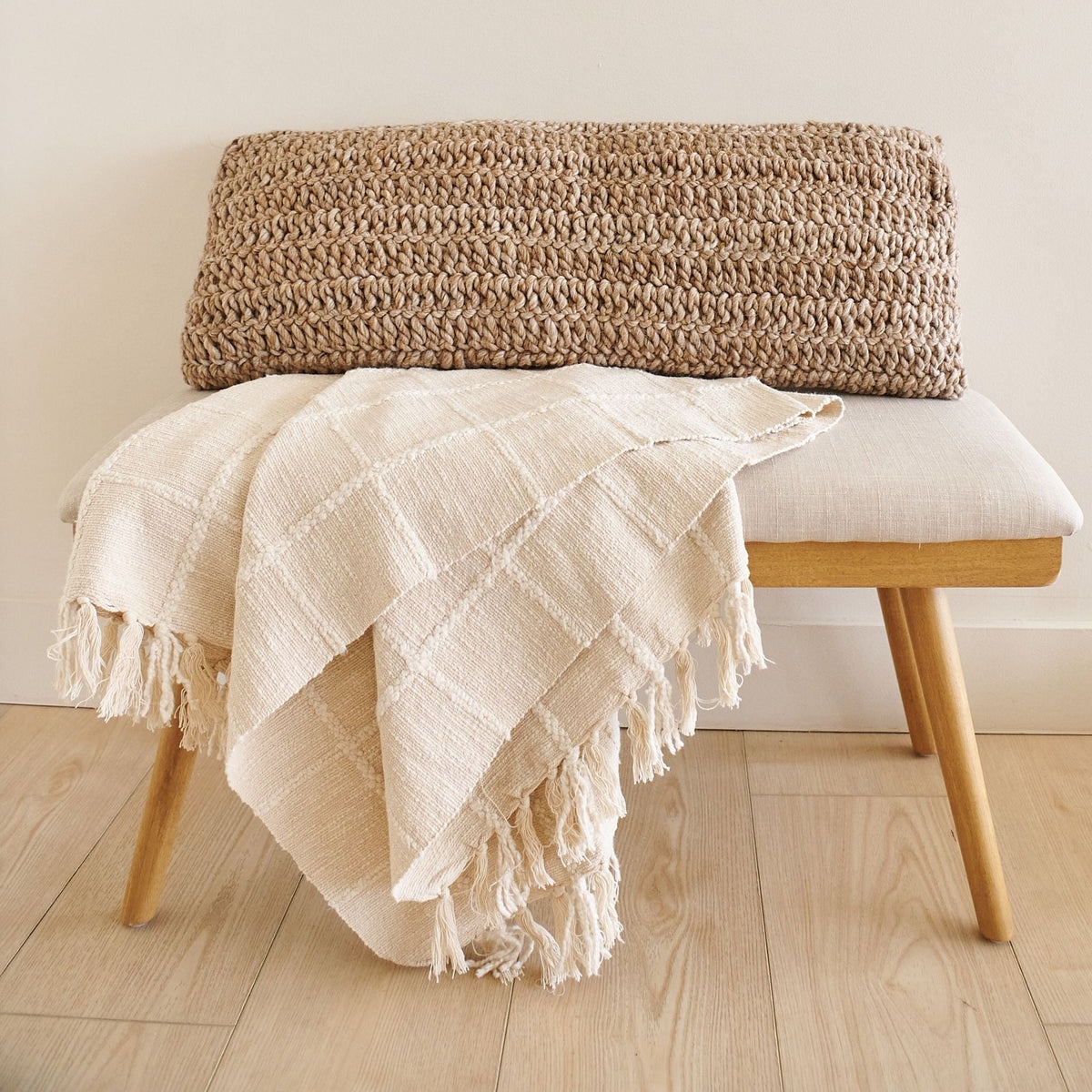 Close view of the Sea Shell White handloom throw cascading over a wood bench beside a chunky brown woven cushion