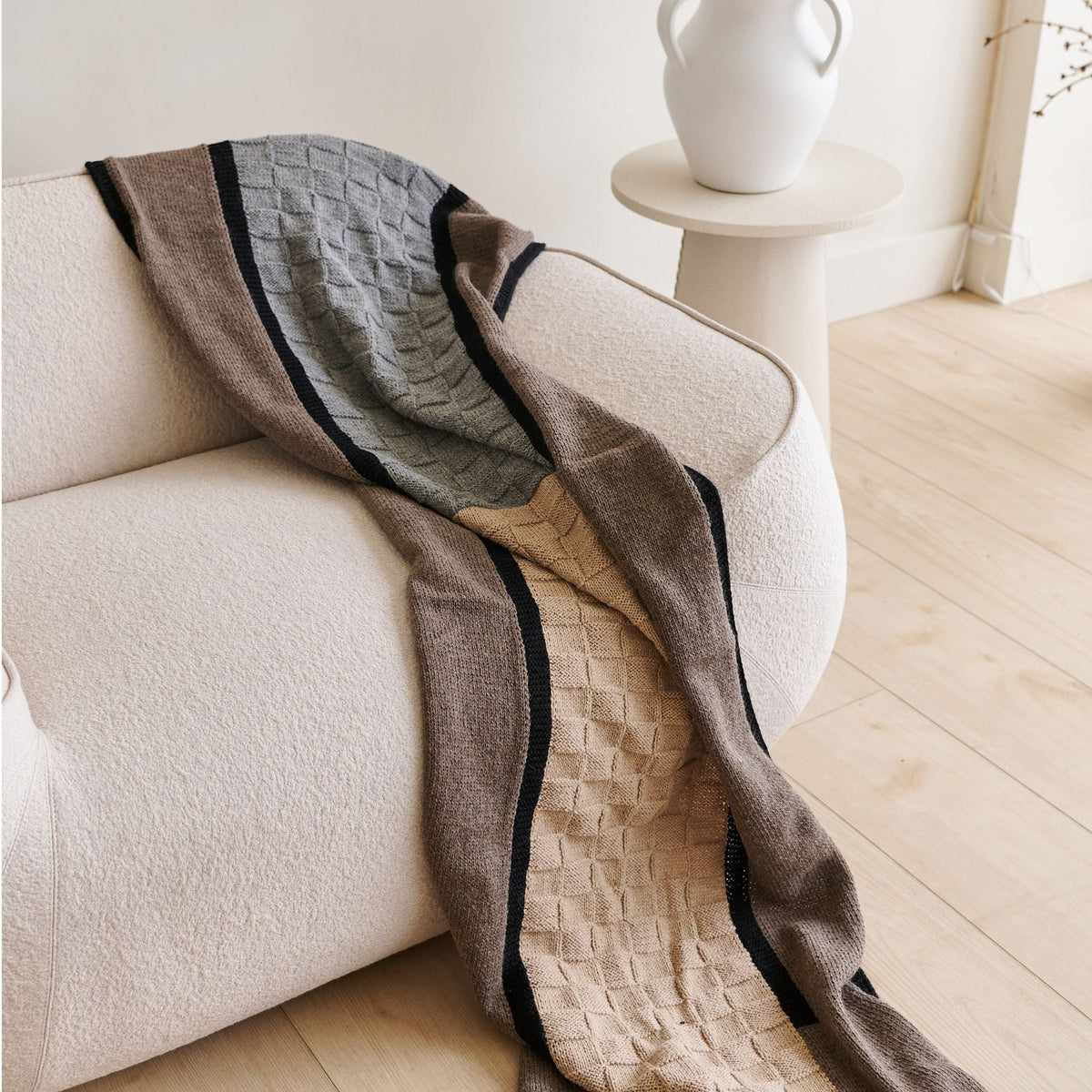 Brown, gray, beige, and black patchwork alpaca blanket draped over a curved cream sofa.
