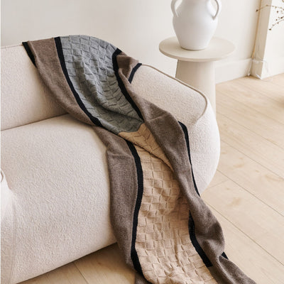 Brown, gray, beige, and black patchwork alpaca blanket draped over a curved cream sofa.