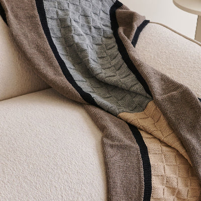Close-up of the gray, brown, and beige knitted panels draped across a textured sofa.