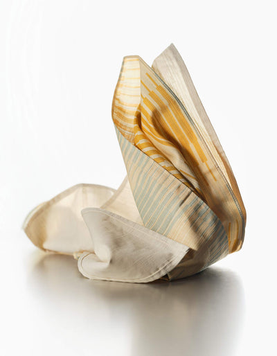 Tortuga Forma Dinner Napkins Double Sided Drift - Quiet Season gathered into upright folds on a light surface, revealing contrasting cream, mustard-yellow and pale grey-green patterned sides and fine woven texture.