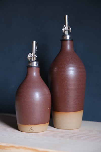 Reddish-brown Settle Ceramics Wander Tall Oil Bottle beside a shorter matching bottle, with softly reflective glaze, visible horizontal rings and pale ceramic bands around the bases.