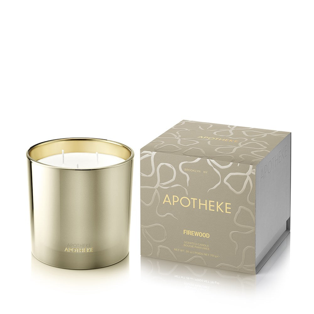 APOTHEKE Firewood 3-Wick Candle in a reflective gold-toned vessel with white wax, beside a matching patterned box with gold lettering on a white background.