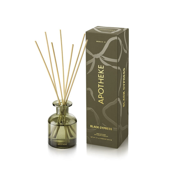 APOTHEKE Black Cypress Mini Reed Diffuser in an olive-green glass bottle with fanned natural-colored reeds, beside a tall olive patterned box with gold lettering on a white background.