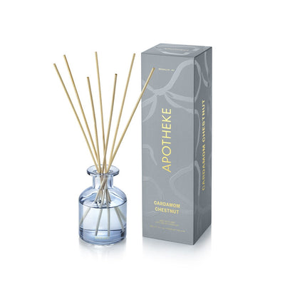 APOTHEKE Cardamom Chestnut Mini Reed Diffuser in a small blue-tinted glass bottle with pale liquid and fanned natural-colored reeds, beside a tall blue-gray patterned box with gold lettering.