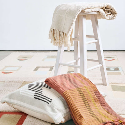 Sea Shell White throw draped over a tall white stool above folded colorful textiles in a styled home decor display