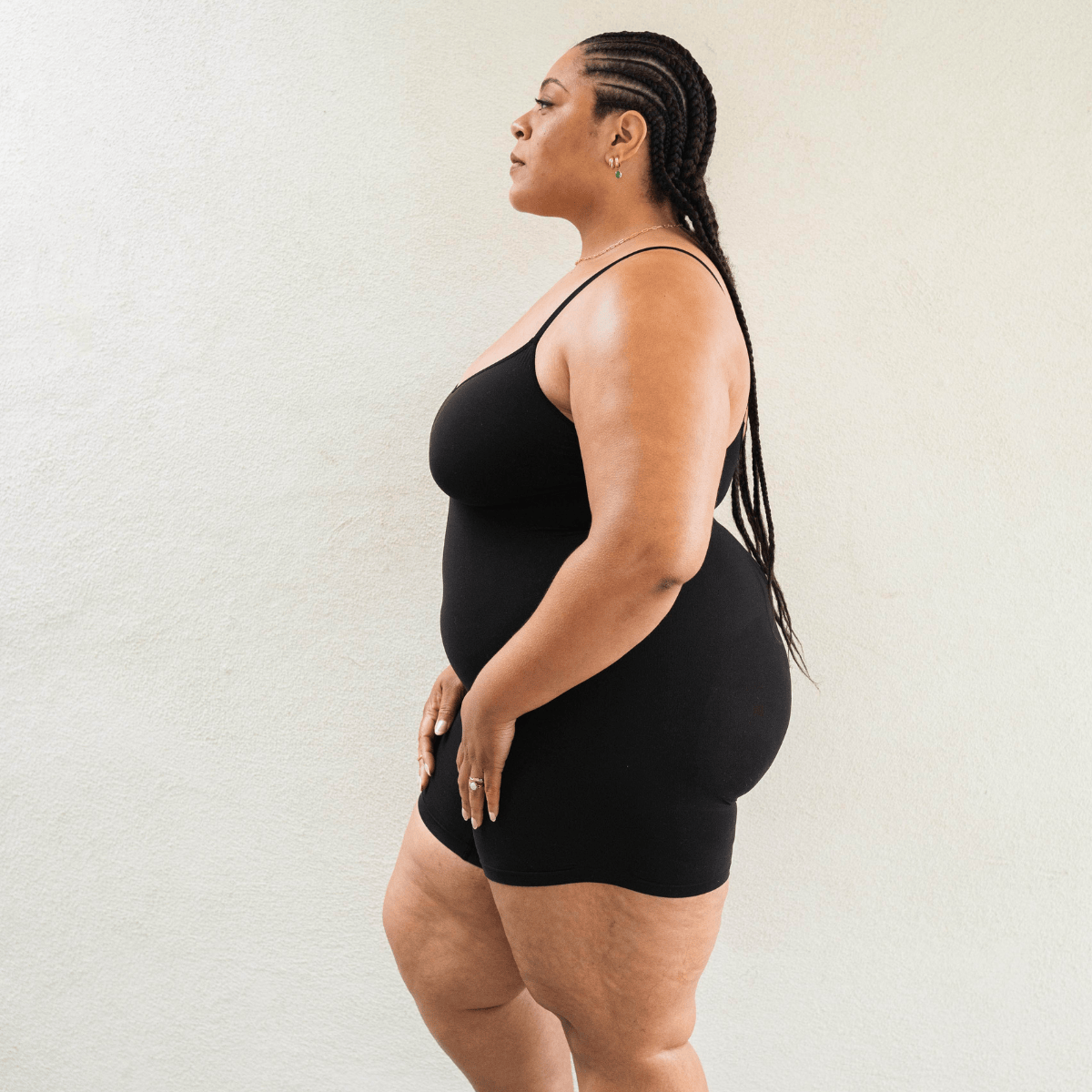 Model wearing PROCLAIM Mid-Thigh Shapewear Bodysuit in Black, side view