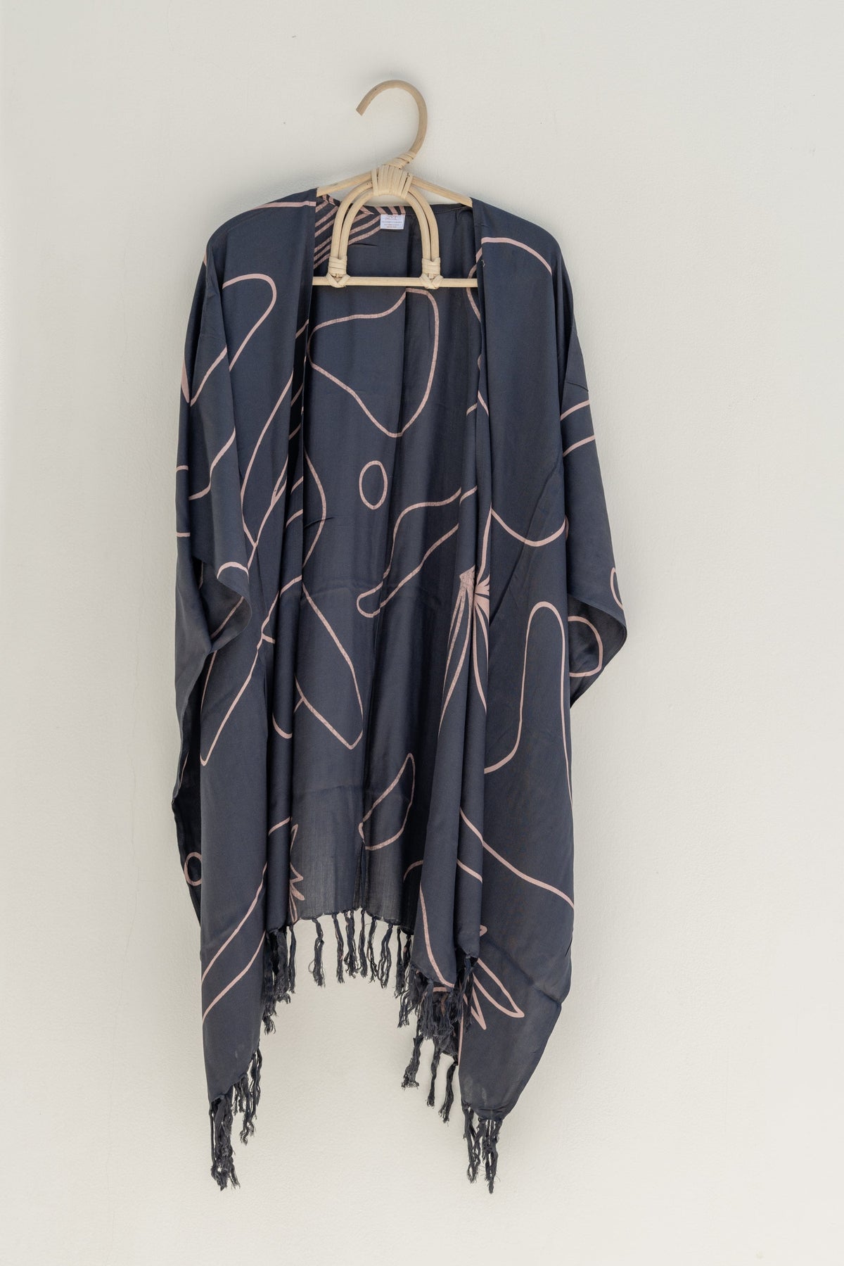 Village Thrive Desert Kimono, charcoal rayon, hanging on a wooden hanger against a plain wall.