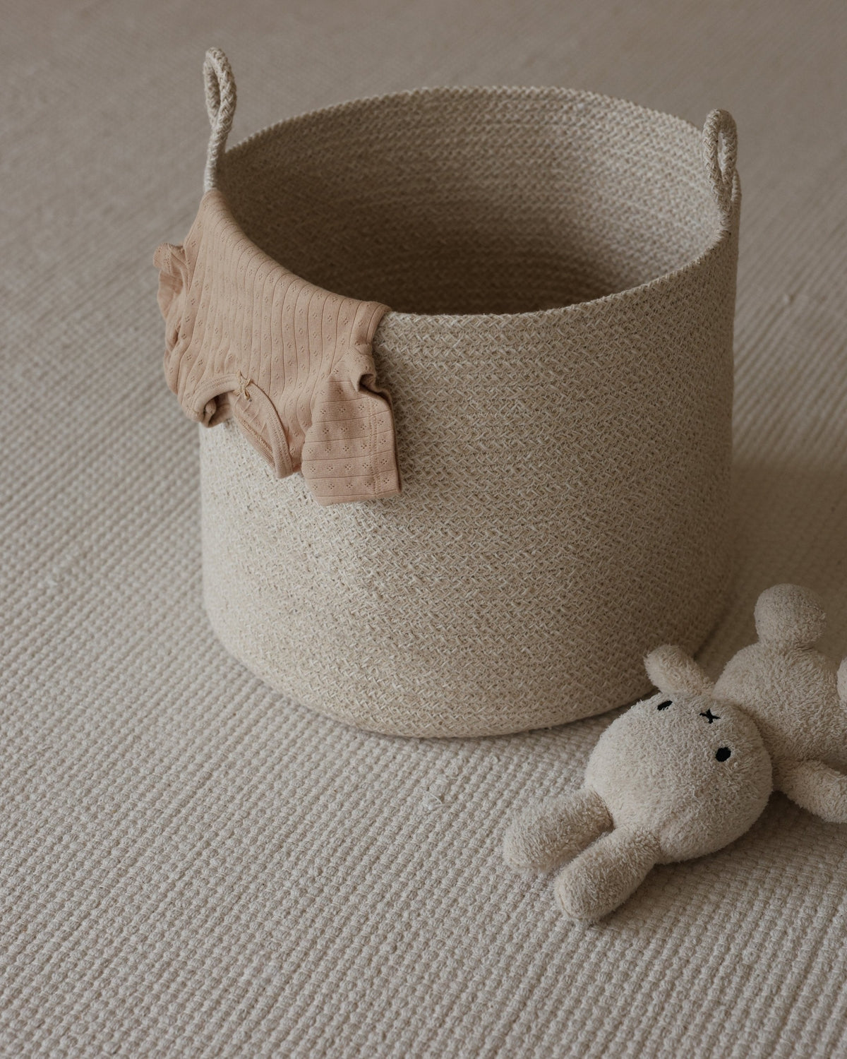 Tall rope basket holding a soft pink textile, styled beside a plush toy.