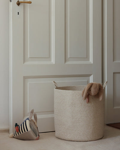 Large beige basket organizing children’s items beside a paneled door.