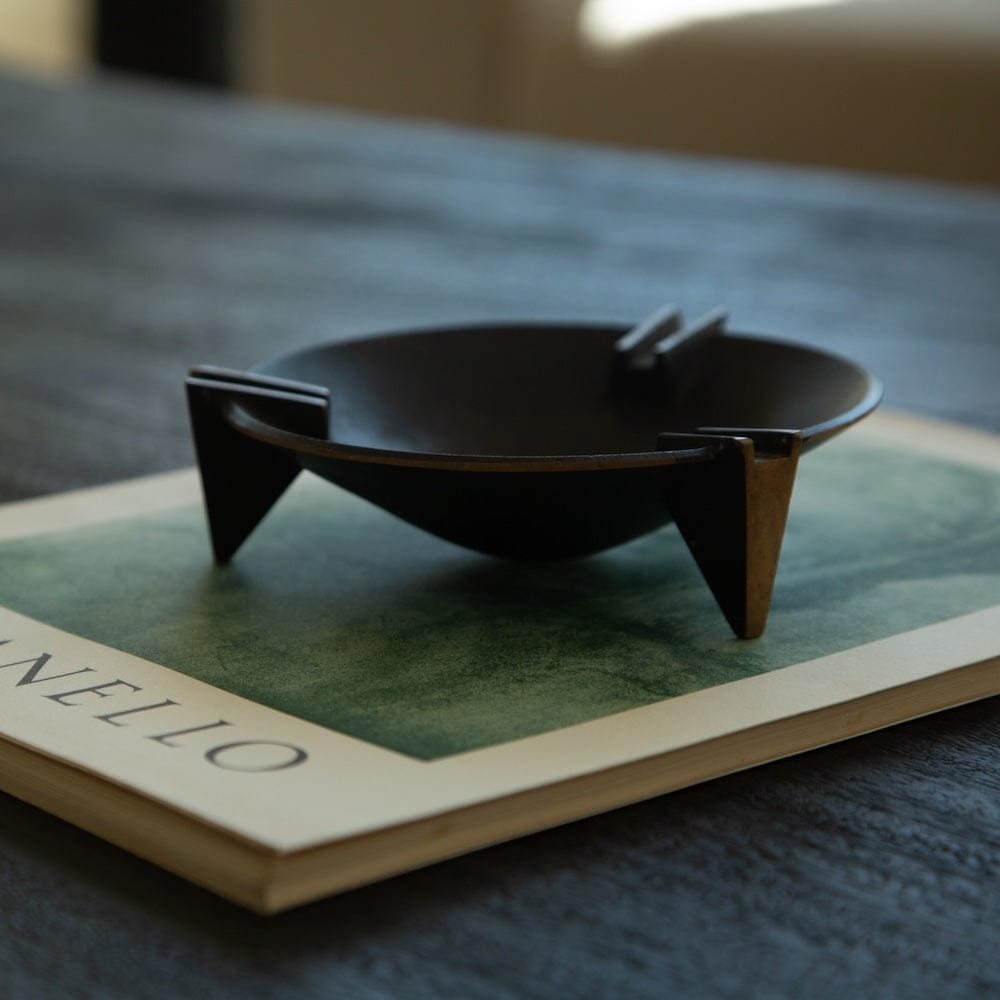 Black Milan ashtray with brass accents displayed on design book