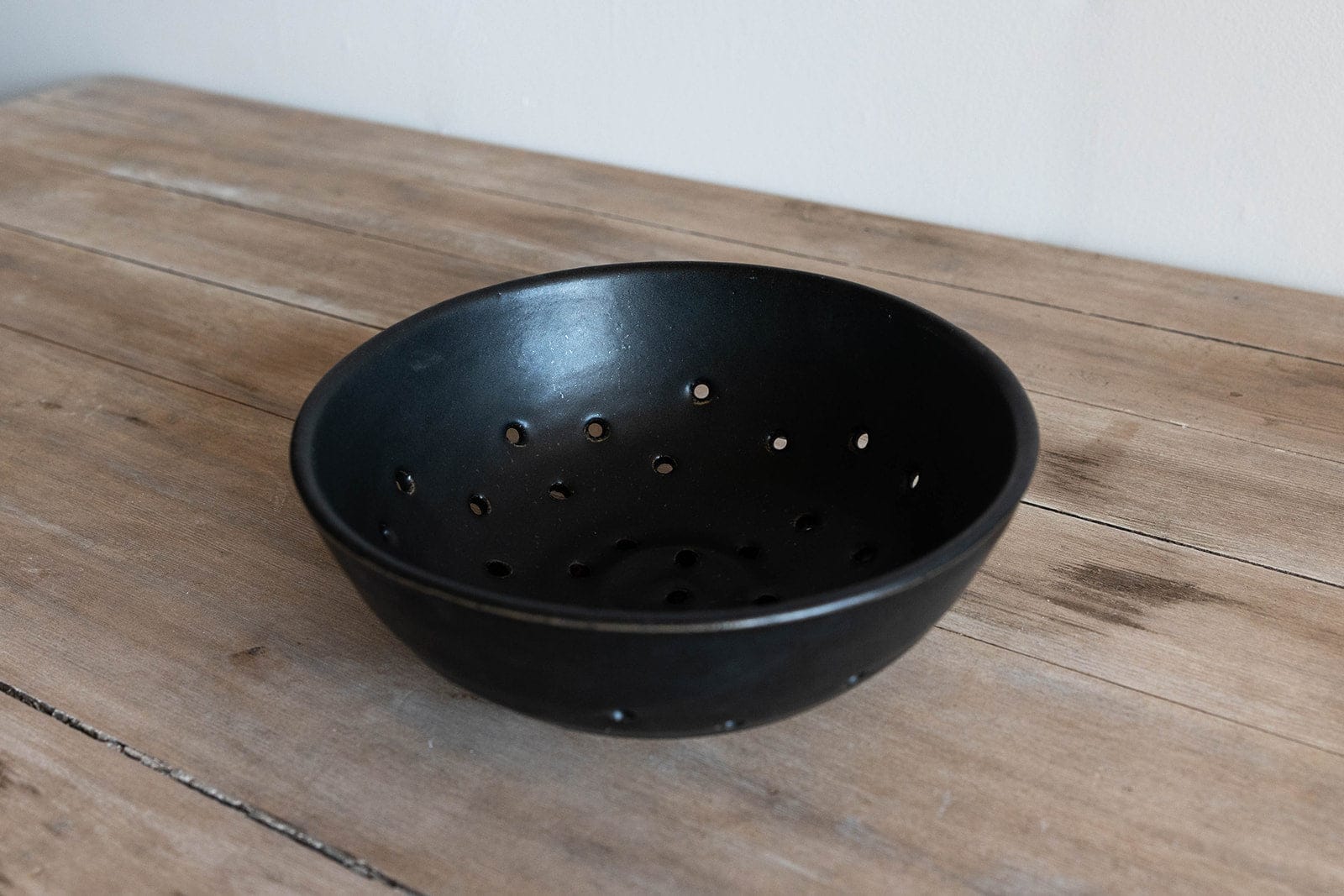 Black perforated ceramic colander bowl on a wooden surface