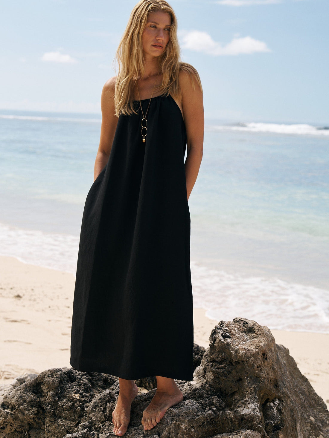Woman in a black dress standing on a beach with ocean in the background
