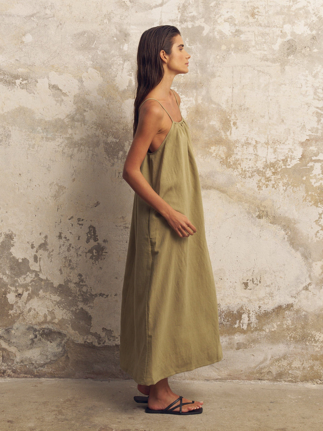 Woman wearing a green dress standing against a textured wall.
