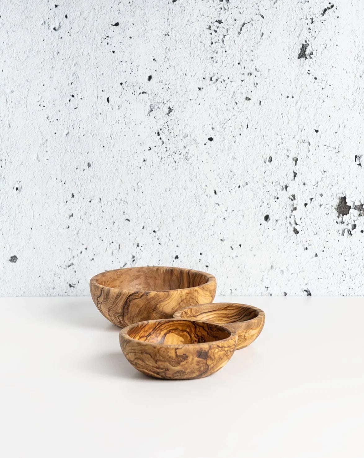Gharyan Stoneware Olive Wood Nesting Bowls, set of 3, against textured wall