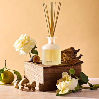 APOTHEKE Cedarwood Ginger Reed Diffuser styled on a wood block with white flowers, ginger root, and a pear