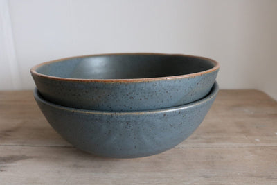 Two blue ceramic bowls stacked on a wooden surface with a white background
