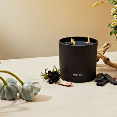 Lit APOTHEKE Charcoal 3-Wick Candle styled with dried florals and driftwood on a light stone surface