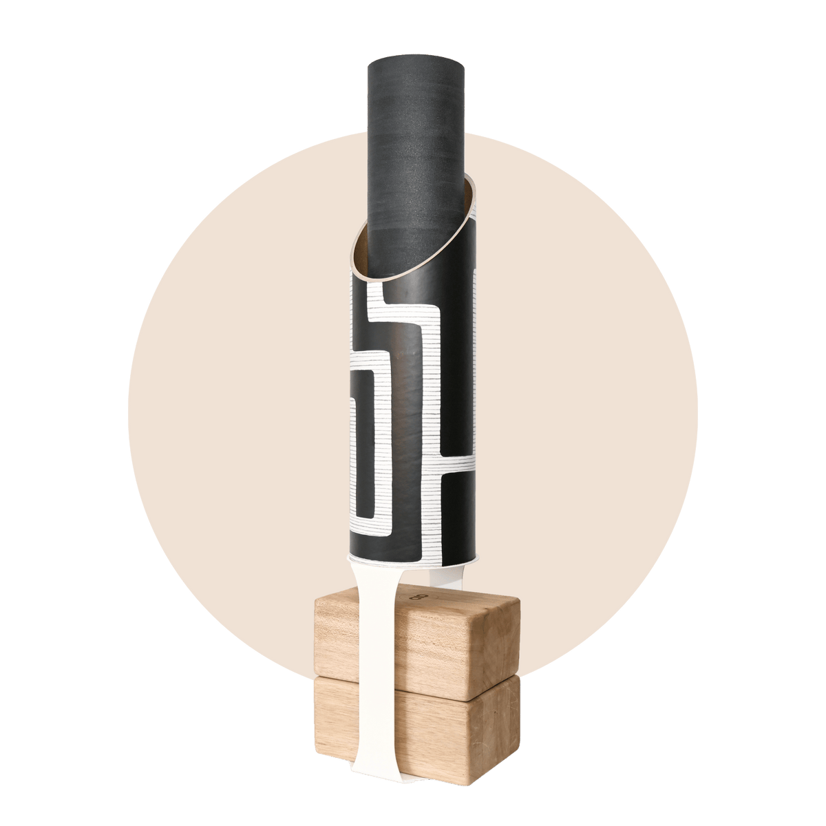 Black cylindrical yoga mat tube with a bold white maze pattern, holding a rolled black mat and standing on four pale wood blocks with a black support strap.