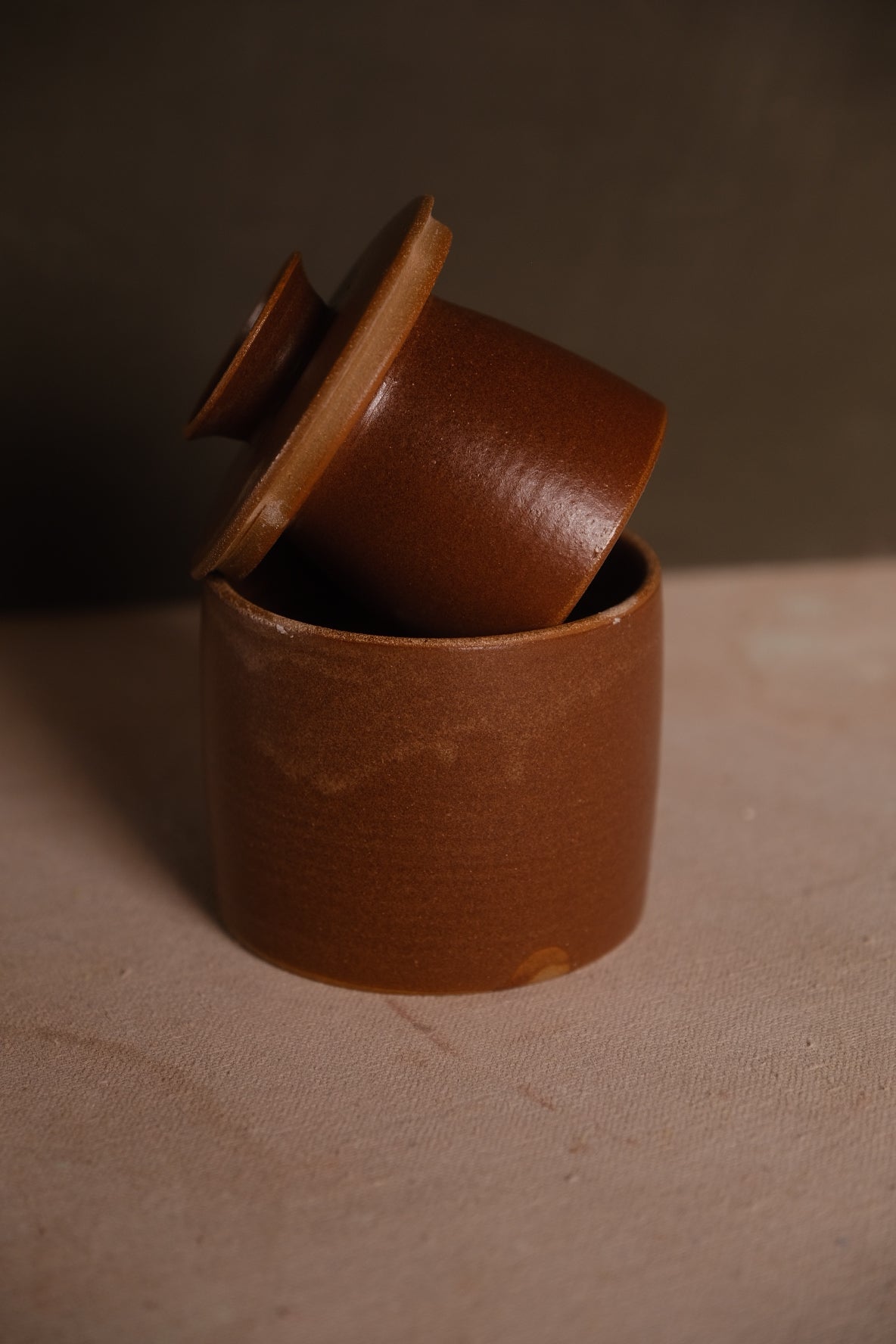 Rust-brown Settle Ceramics Butterbell displayed partly open, showing a rounded lid knob, broad ochre rim and softly varied glaze across the cylindrical base.