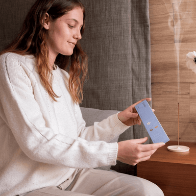 Woman seated indoors opening a light blue box of Looshi Change incense sticks beside a wooden table