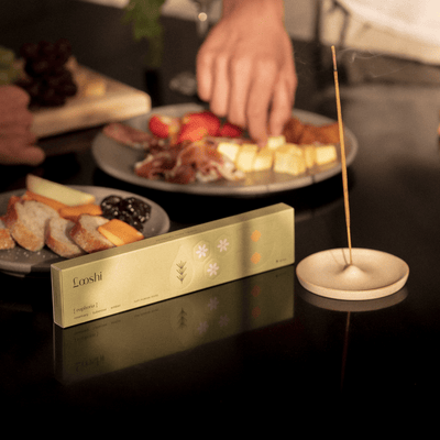 Looshi Euphoria incense box and a burning incense stick arranged beside plates of food as a person reaches across the table