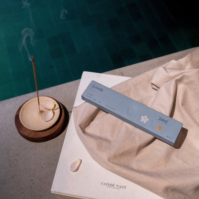 Looshi Calm incense box and a burning incense stick arranged on cream fabric beside a turquoise swimming pool