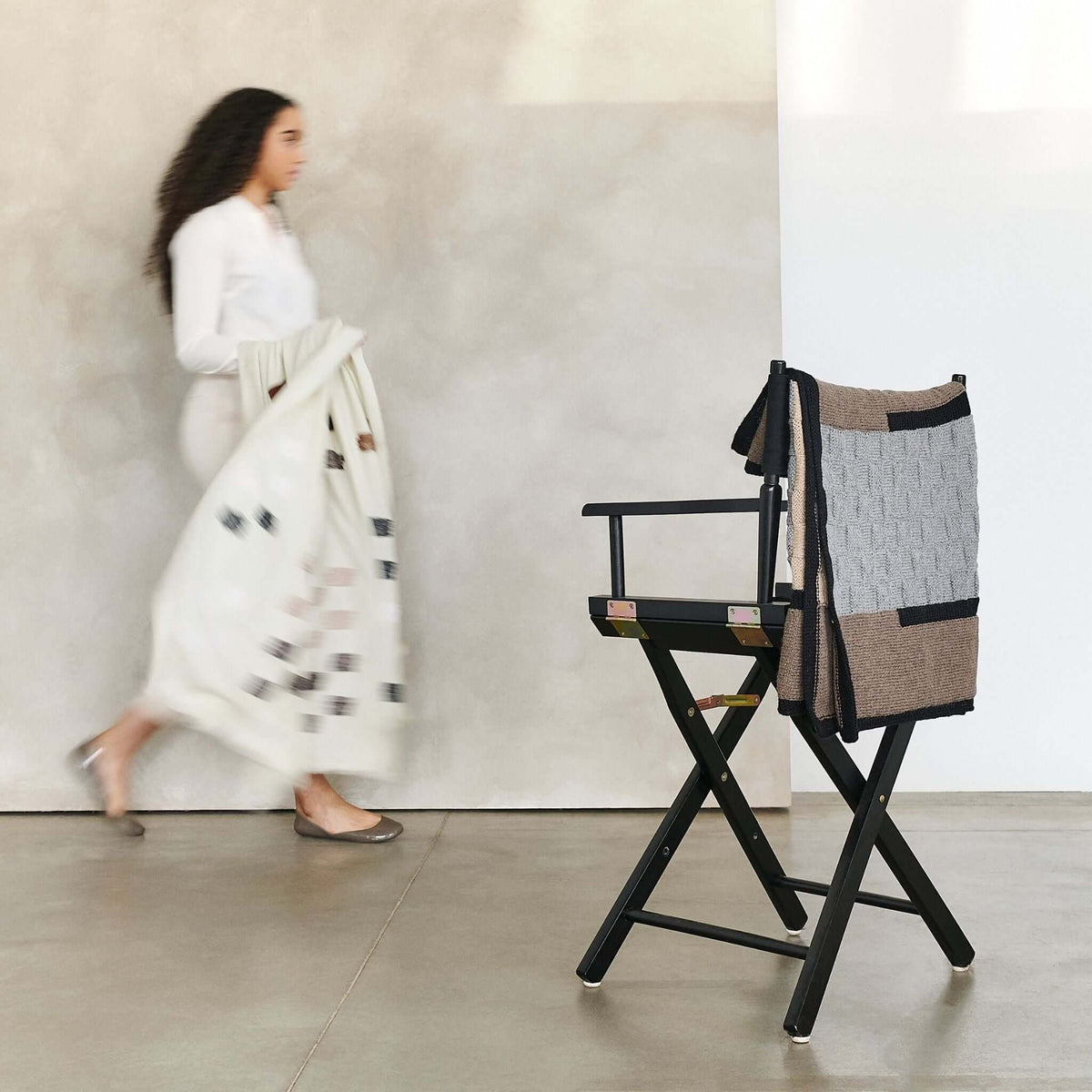 Woman walking past a chair draped with the Muhu blanket in a minimalist studio.