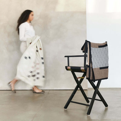 Woman walking past a chair draped with the Muhu blanket in a minimalist studio.