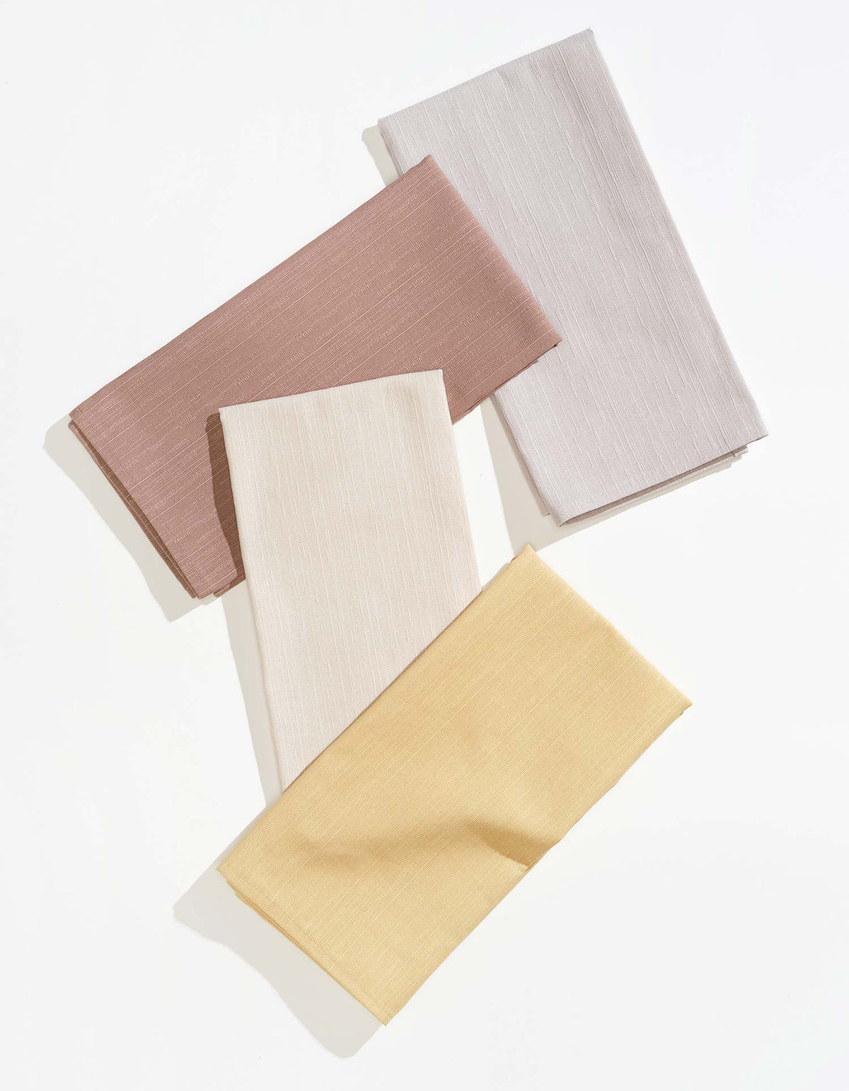 Four Tortuga Forma Dinner Napkins Sabi Mixed Sets in dusty rose, pale grey, ivory and soft yellow, folded into overlapping rectangles on white, showing fine woven texture and neatly stitched hems.