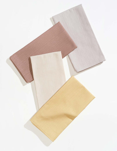 Four Tortuga Forma Dinner Napkins Sabi Mixed Sets in dusty rose, pale grey, ivory and soft yellow, folded into overlapping rectangles on white, showing fine woven texture and neatly stitched hems.
