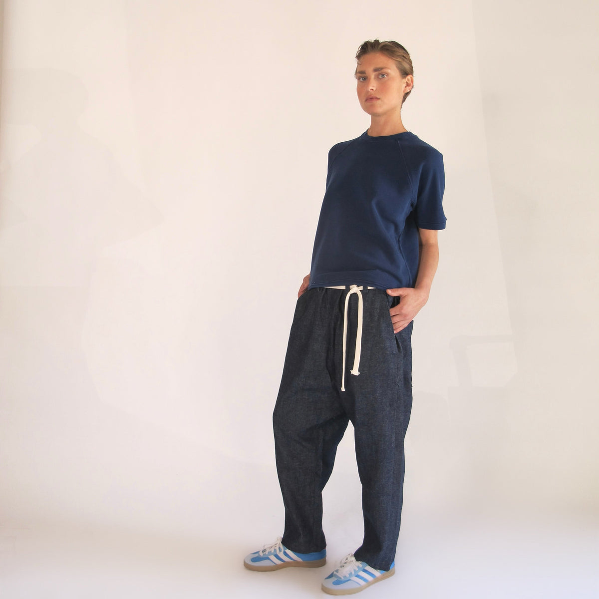 Model wearing a navy raglan shirt with loose black drawstring pants and blue sneakers.