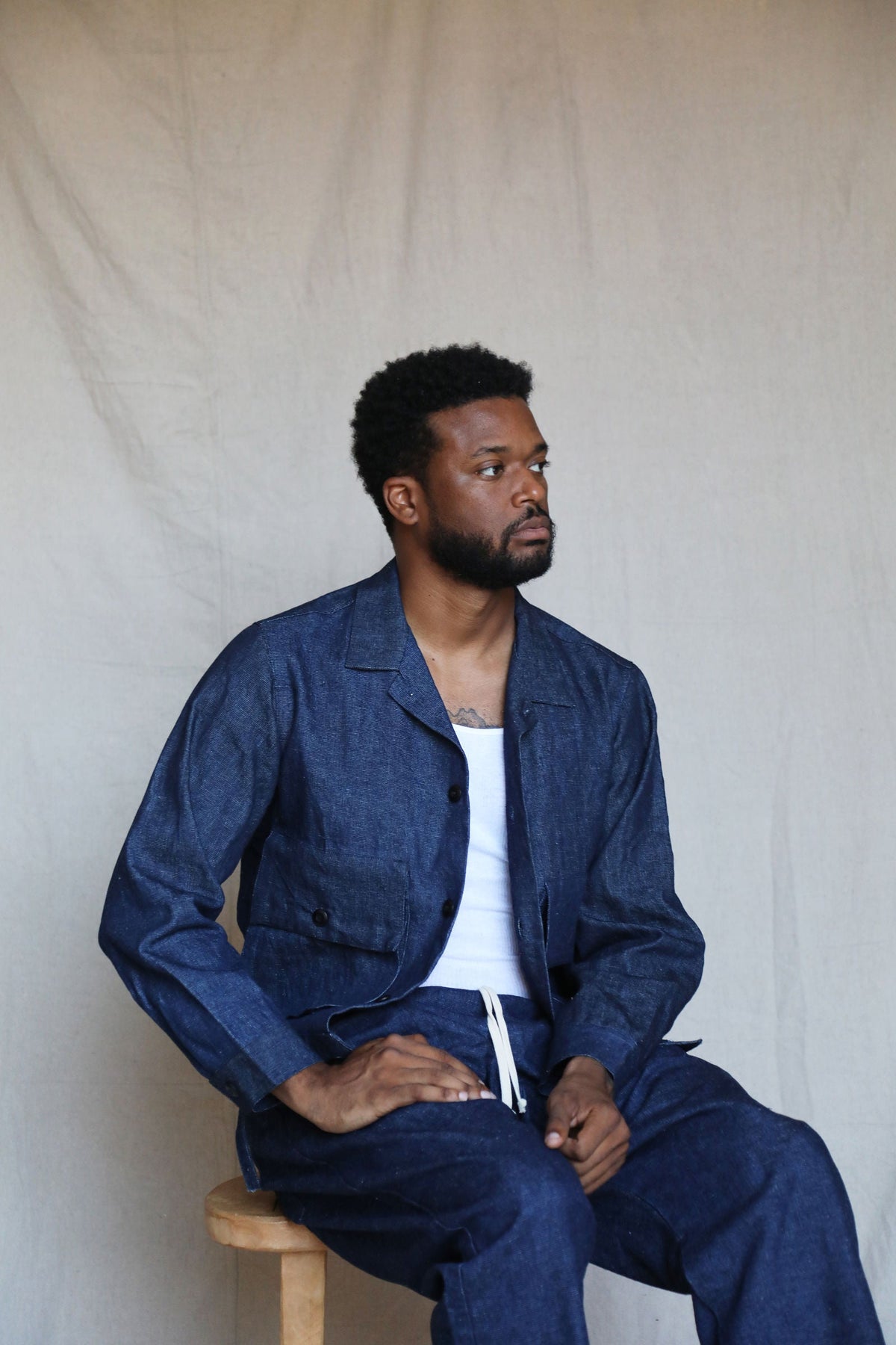 Seated model wearing the indigo Studio Coat, white shirt, and matching pants.