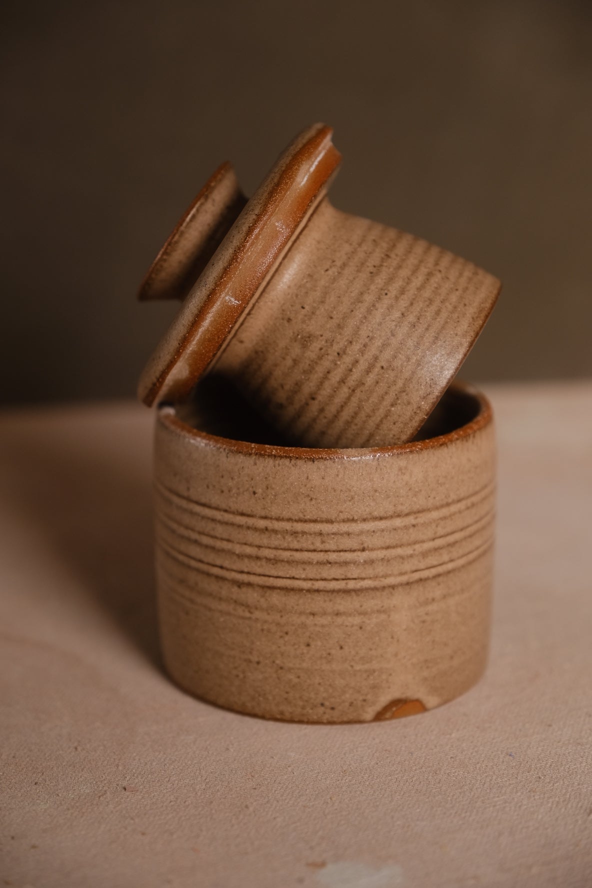 Sandy-beige Settle Ceramics Butterbell with closely spaced horizontal ridges around both the base and tilted inner cup, framed by a warm brown lid rim.
