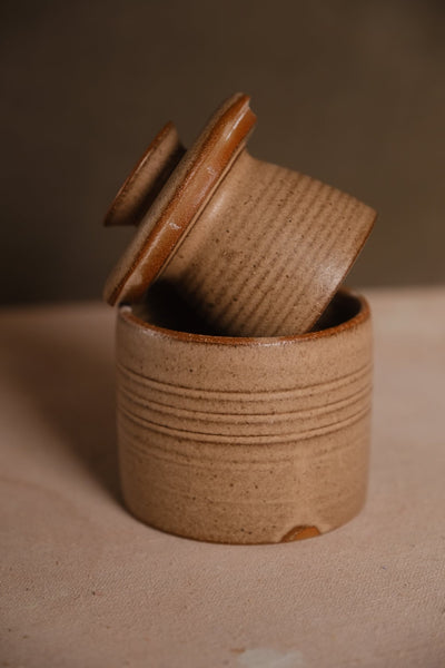Sandy-beige Settle Ceramics Butterbell with closely spaced horizontal ridges around both the base and tilted inner cup, framed by a warm brown lid rim.