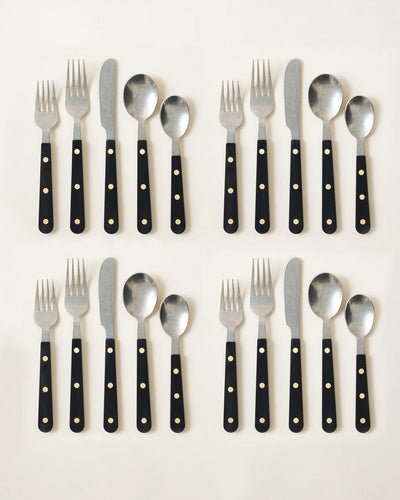Two complete black-handled cutlery settings arranged in rows, with polished metal utensils and three bright rivets on each handle.