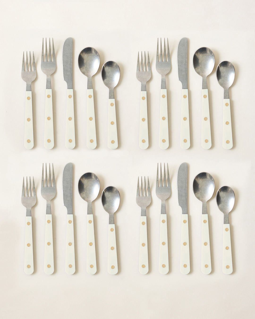 Two complete ivory-handled cutlery settings arranged in neat rows, showing polished stainless-steel utensils and warm cream handles with brass-toned rivets.