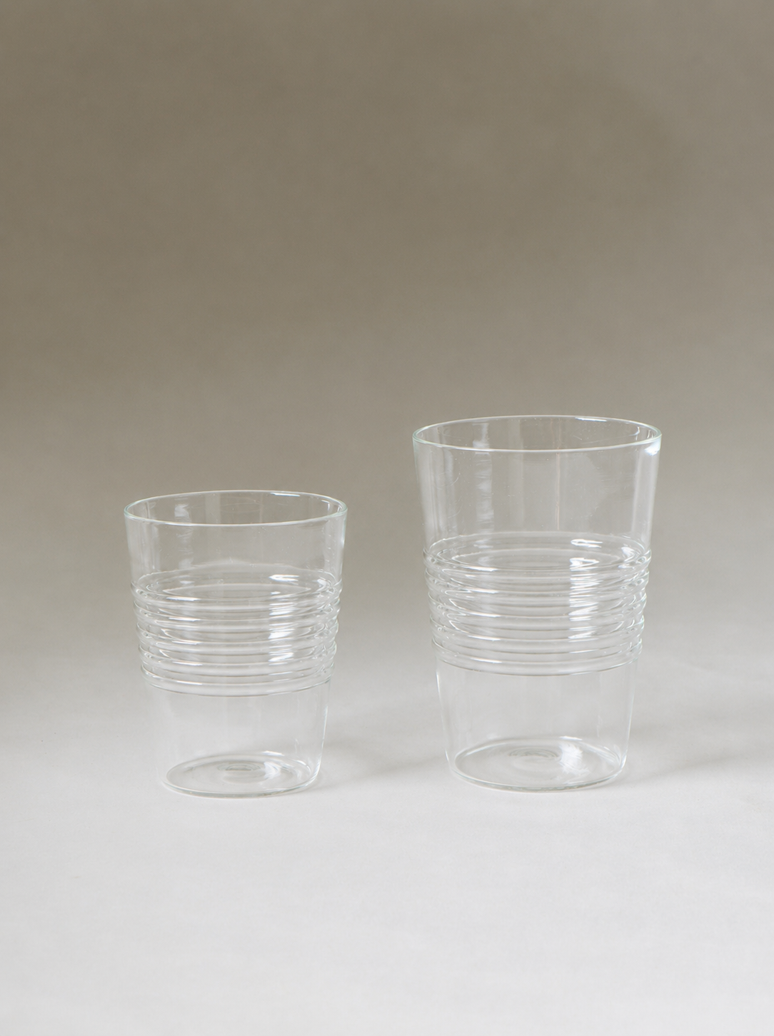 Two empty clear tumblers in different sizes, each detailed with horizontal ridges around the lower half.