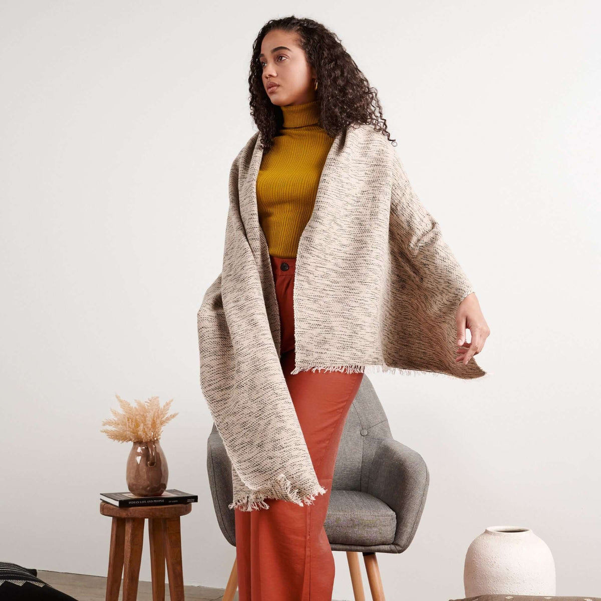 Woman standing in a mustard top and rust trousers with the oversized scarf draped over one shoulder.
