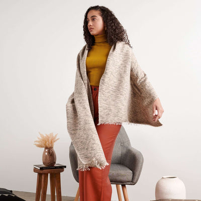 Woman standing in a mustard top and rust trousers with the oversized scarf draped over one shoulder.