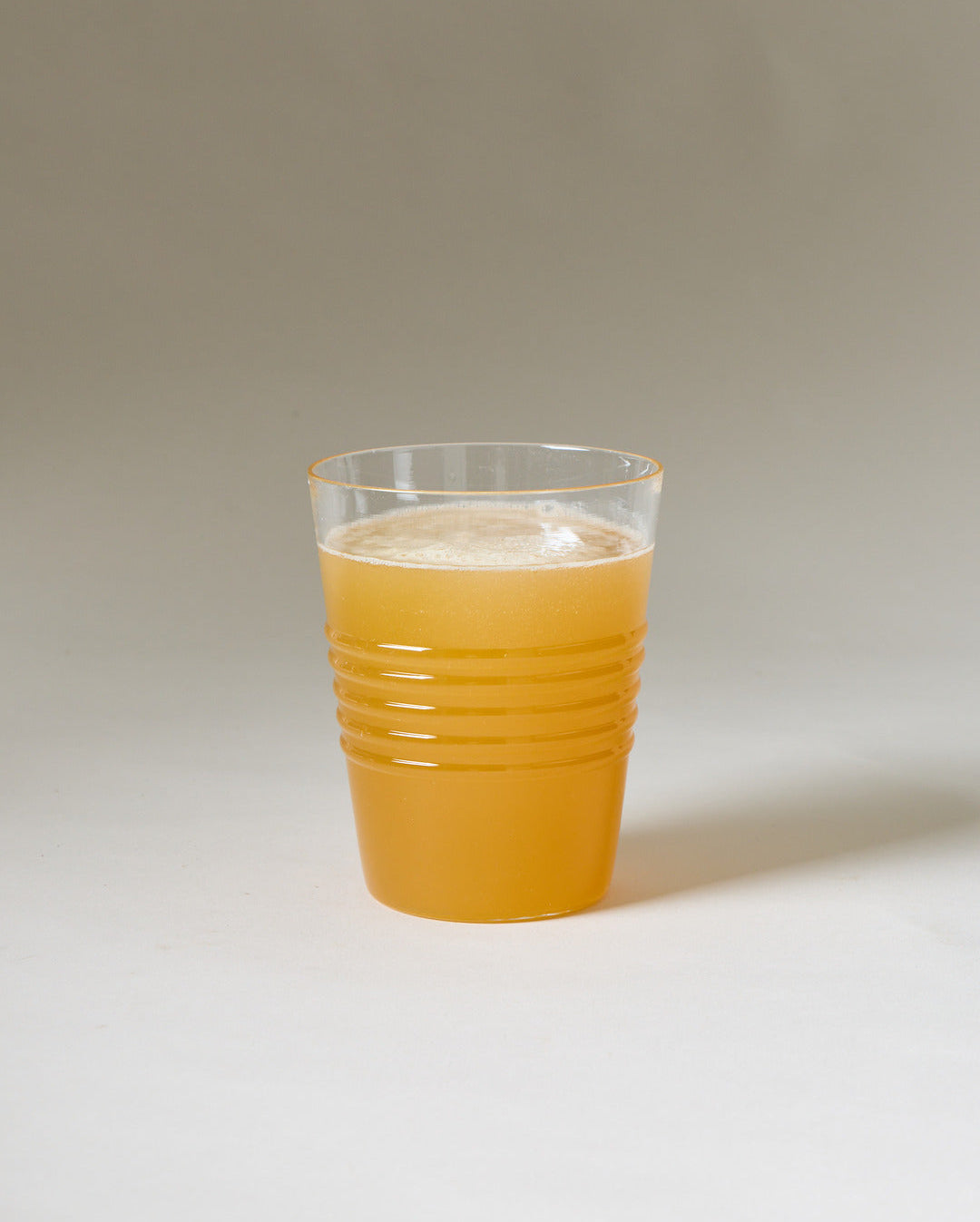 Clear ridged tumbler filled with opaque orange juice against a neutral studio background.