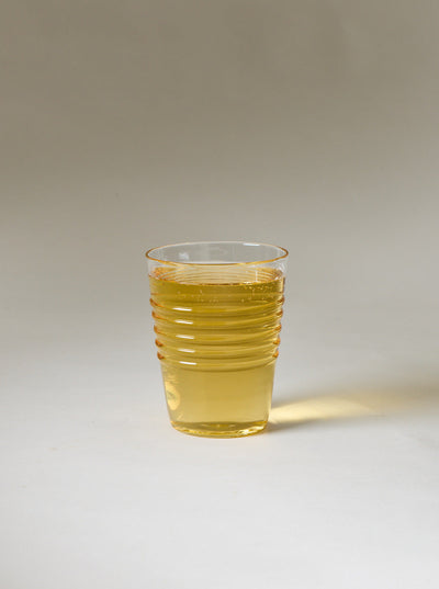 Small clear ridged glass filled with a translucent golden drink against a neutral studio background.