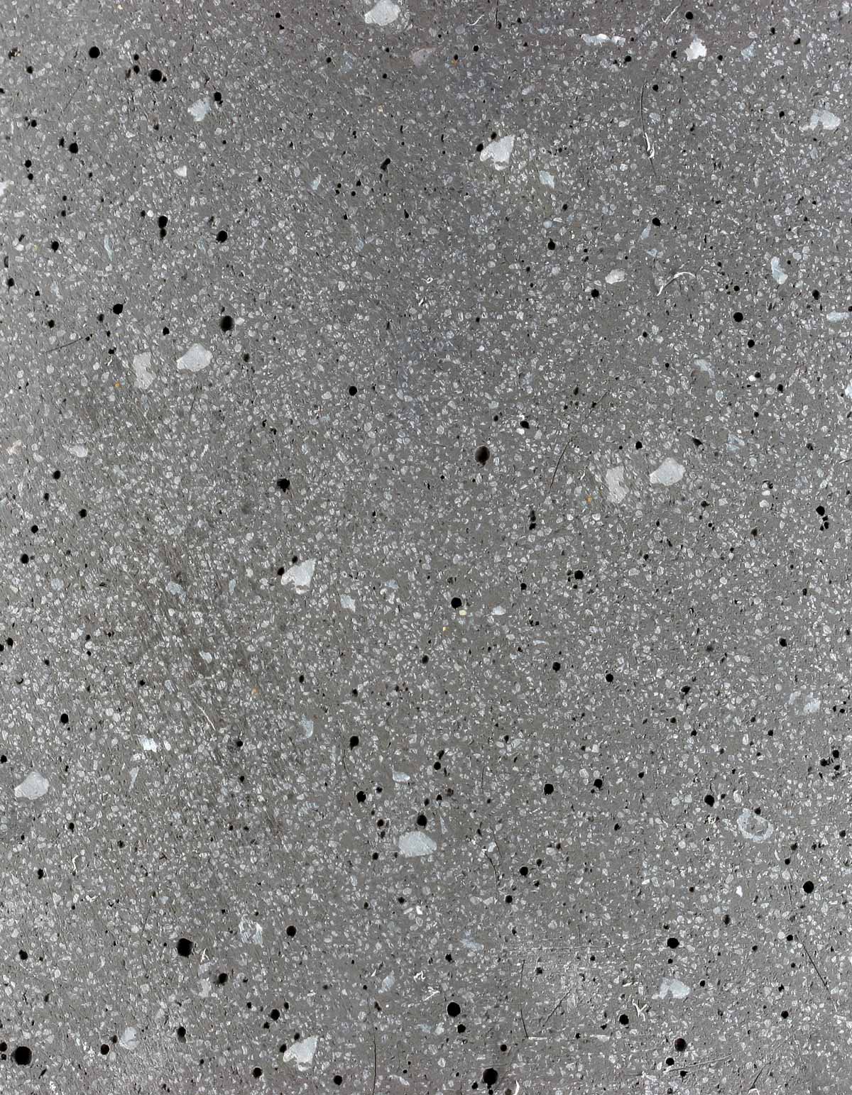 Close-up of the graphite finish on the Tortuga Forma Platform Planter Small - Terrazzo, showing irregular white, light grey and black chips embedded in a grey background.