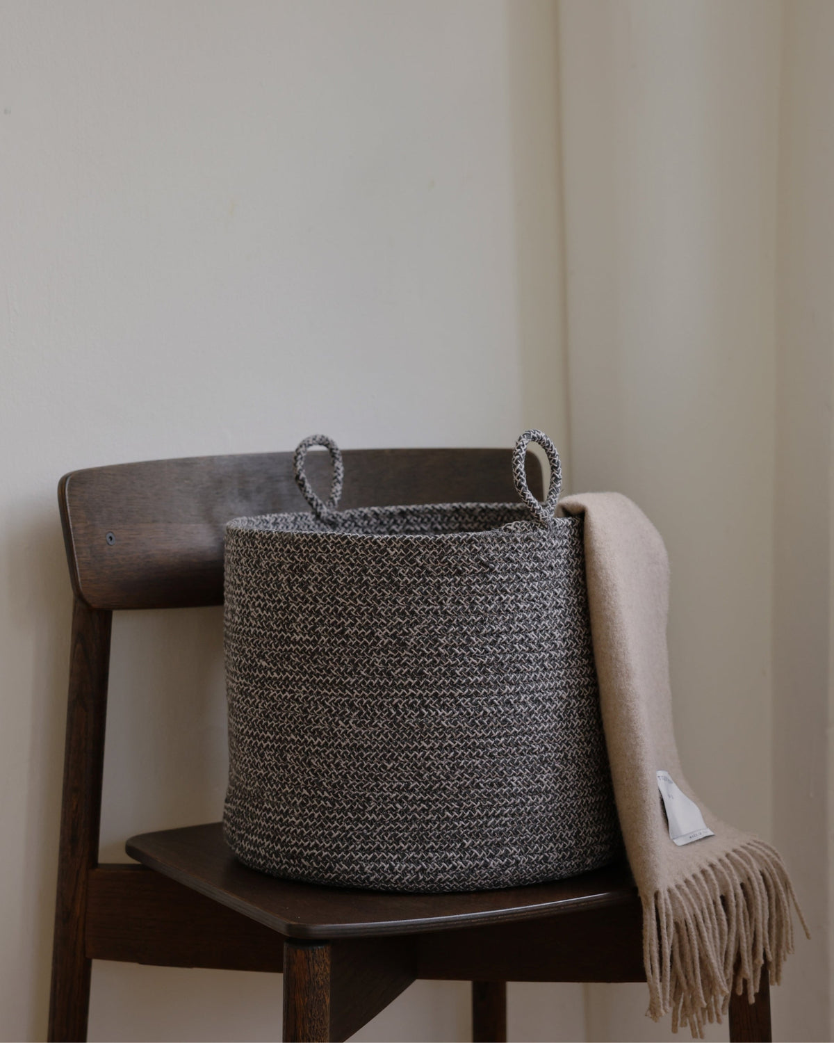 Gray melange basket styled on a wooden chair with a light throw draped beside it.