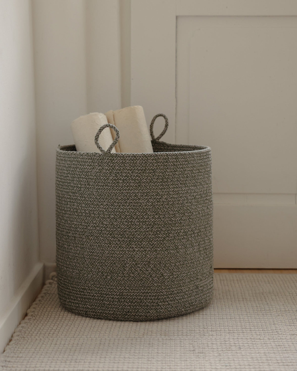 Large green melange basket holding rolled papers in a softly lit room.